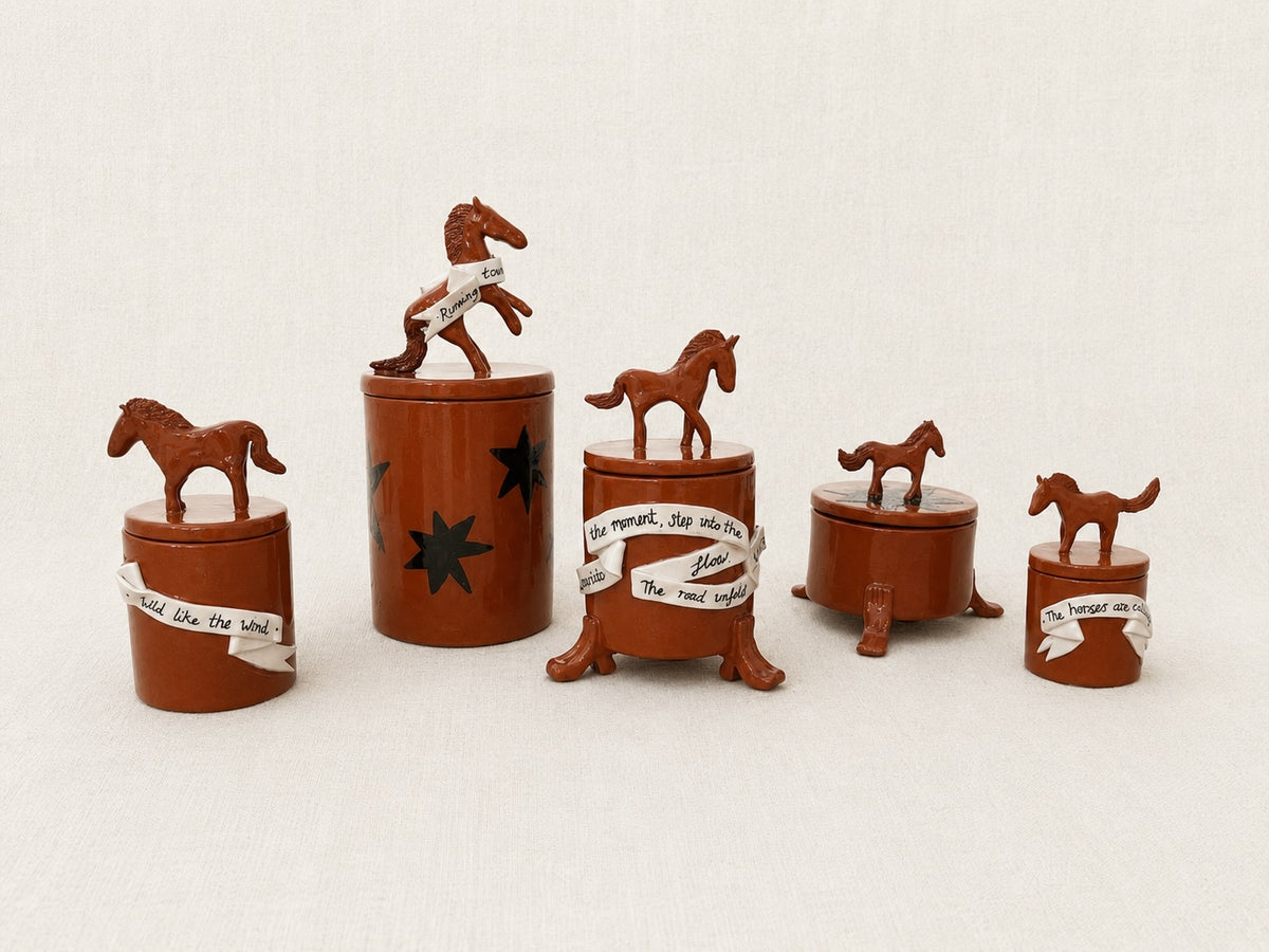 Five small brown wooden horse-themed artisan ceramic lidded jars. Handmade terracotta jars with sculpture horses on top and added illustrations and ribbons of poetry.