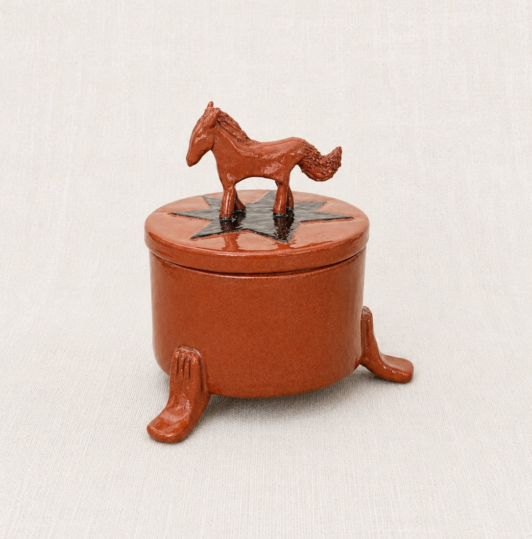 A small round terracotta decorative box with a lid, featuring a horse figurine on top and three short legs.