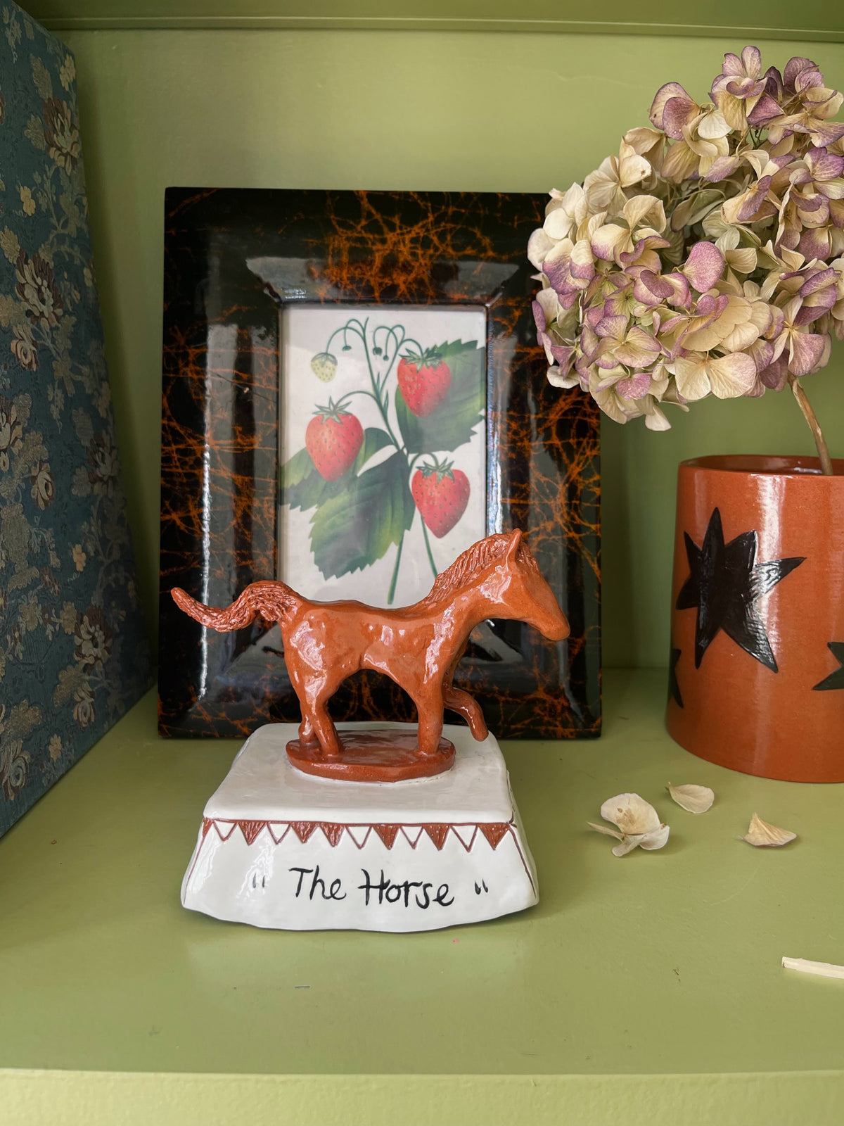 A small terracotta-colored horse figurine standing on a white base labeled "The Horse," 